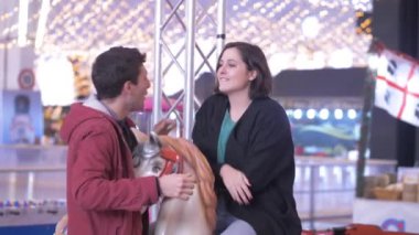 Gülümseyen genç çift Noel zamanı atlıkarıncada konuşuyor ve şakalaşıyor.