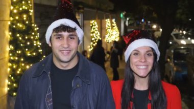 Gençlik, mutluluk - Noel Baba şapkası takan genç bir çift - gece kamera sahnesinde gülümsüyor