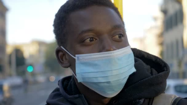 バスの停留所にマスクをした若い思慮深い黒人男性が周りを見回し — ストック動画