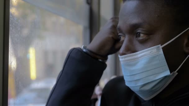 マスク付きバスで マスク付きの疲れ黒い男は窓の外を見る — ストック動画