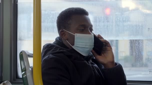 マスクをつけて電話で 退屈そうに見える電話でバスにマスクをした黒人男性 — ストック動画