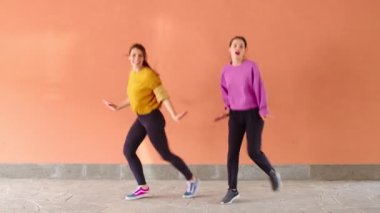 İki genç kadın kameranın önünde senkronize dans çalışıyor.