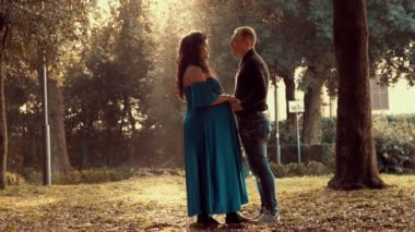 Parkta bir çift müstakbel ebeveyn el ele tutuşup birbirlerinin gözlerine bakıyorlar. 