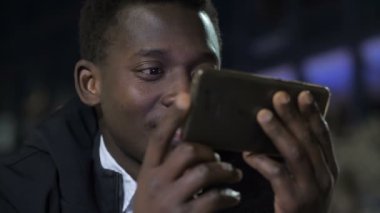 Teknoloji, uygulama. Genç siyahi adam gülümsüyor. Telefonundaki videoyu izlerken eğleniyor.