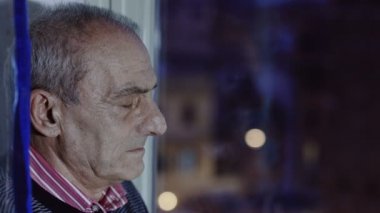 gece şehir ışıkları arka planda ile pencereden dışarı bakarak eski depresif adam