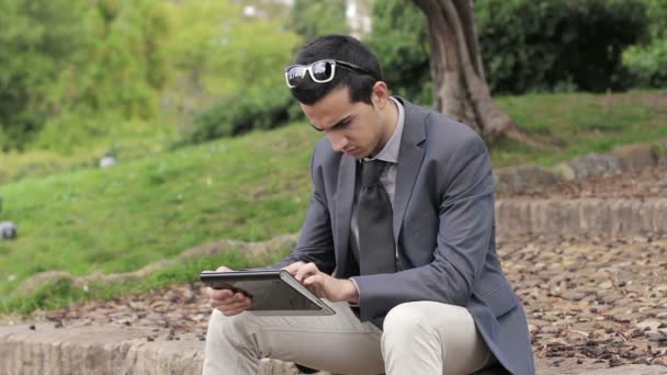 Empresario en el parque con la tableta sentada en un banco — Vídeo de stock