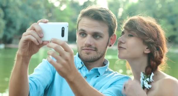 Joven pareja enamorada haciendo selfie cerca de un pequeño lago dentro de un jardín público — Vídeo de stock