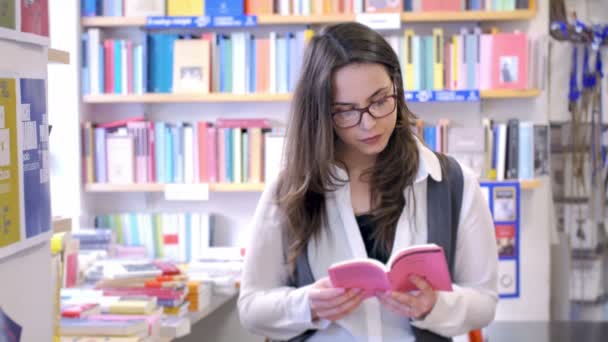 Красива молода жінка читає книгу в книгарні і шукає нову книгу — стокове відео