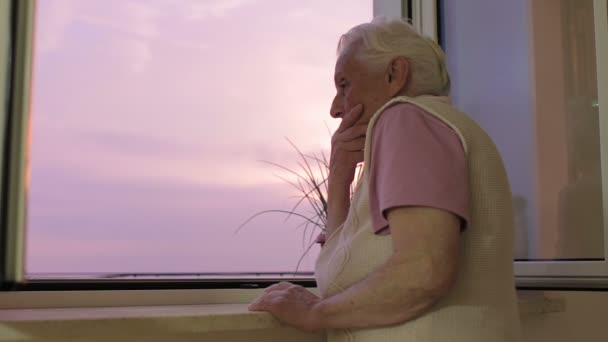 Treurig en eenzaam oude vrouw kijkt uit raam - depressief - zonsondergang — Stockvideo