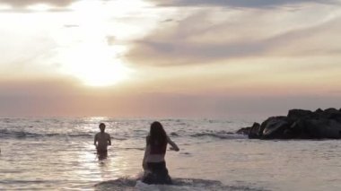 Kız aşık sevgilisi deniz - hugs ve öper - gün batımına doğru çalışır.