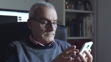 düşünceli yaşlı adam dokunmatik ekranlı akıllı telefon kullanıyor