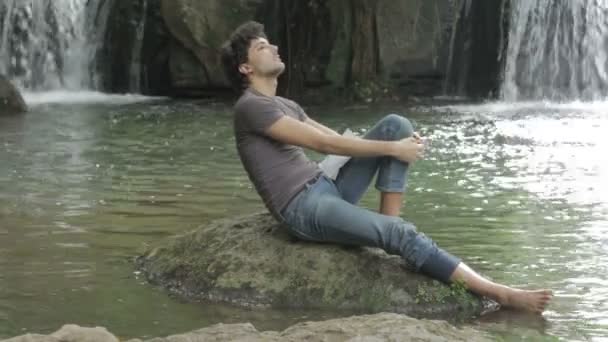 Hombre guapo se relaja en la roca — Vídeo de stock