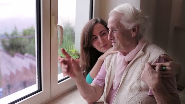 Oma en kleindochter ontspannen in de buurt van Windows bij zonsondergang thuis - knuffel — Stockvideo