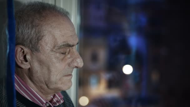 Вдумчивый старик у окна вечером — стоковое видео