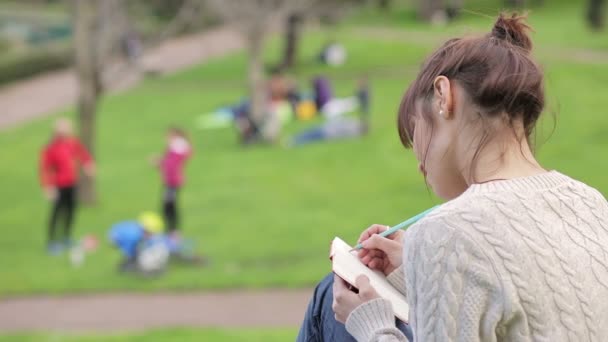 Beautiful young woman is writing a diary outdoors in the park: — Stock Video