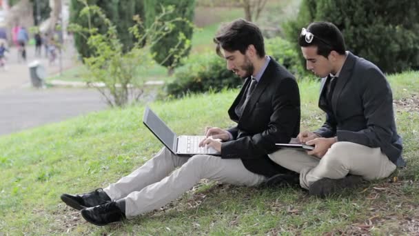 Zwei Geschäftsleute mit Tablet und Laptop sprechen über ein Projekt im Park — Stockvideo