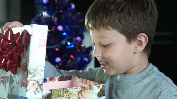 Niño feliz abre un hermoso regalo de Navidad en una caja — Vídeos de Stock