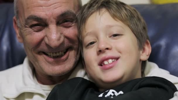 Abuelo y nieto en el sofá riendo y mirando a la cámara — Vídeos de Stock