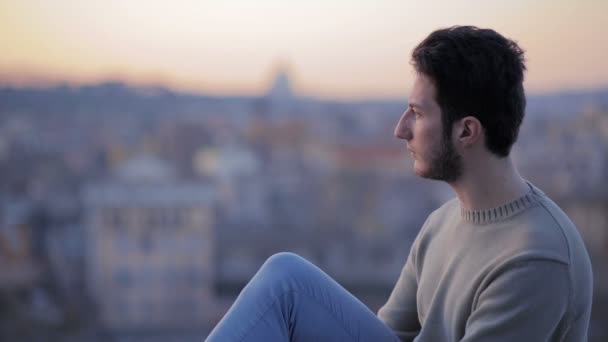 Young man sitting, looks upset. Man in front of Rome landscape — Stockvideo