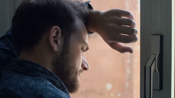 Portrait d'un beau jeune homme triste devant une fenêtre. 4k — Video