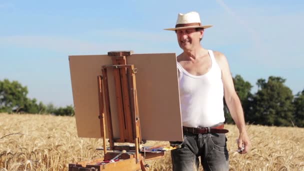 Живописець з мольбертом посеред пшеничного поля — стокове відео