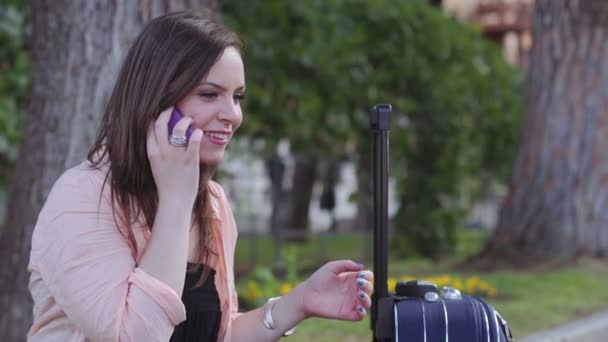 Uma jovem mulher com uma mala está ao telefone e ela está rindo com alegria — Vídeo de Stock