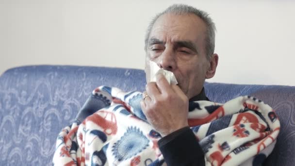 Άρρωστος άνθρωπος με ένα κρύο κάθεται στον καναπέ με μια κουβέρτα — Αρχείο Βίντεο