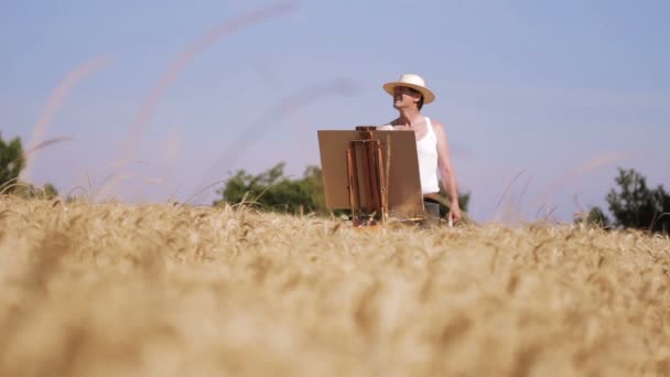 Schilder in het midden van een tarweveld schildert een prachtig landschap, borstel — Stockvideo