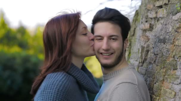 Nettes Mädchen küsst hübschen jungen Mann, der sich an einen Baum lehnt: Liebe, Spaß, Jugend — Stockvideo