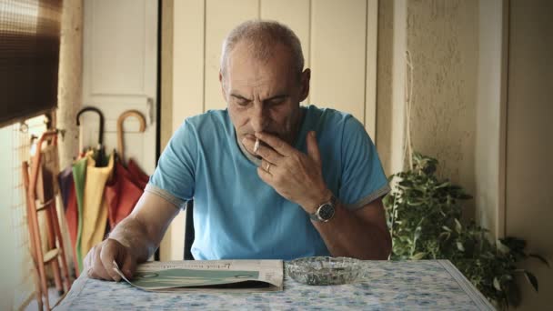 Äldre man läser tidningen hemma och röker cigarett: 4 k film — Stockvideo