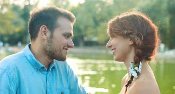 Young couple kissing in front of small lake in a public garden: romantic date — Stockvideo