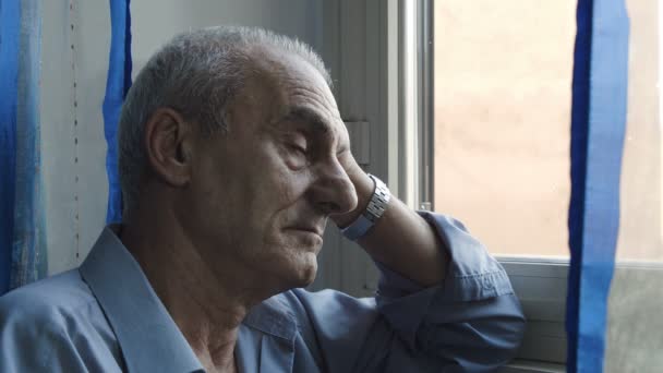 Viejo deprimido en la ventana está mirando hacia fuera y pensando — Vídeos de Stock