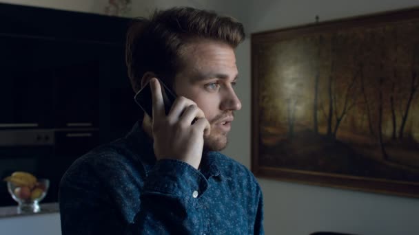 Guapo joven responde al teléfono en su casa: teléfono inteligente, 4k — Vídeos de Stock