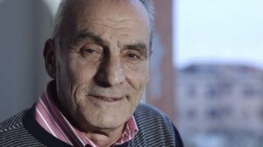 huzurlu yaşlı adam kameraya arka planda bir pencere ile gülümseyen