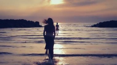 aşık giyimli kadın erkeğini için deniz - hugs ve öper - gün batımına doğru çalışır.