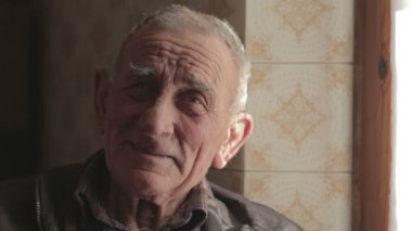 Kameraya bakarak gülümseyen yaşlı adam