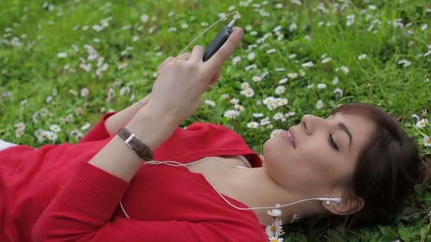 Όμορφο κορίτσι χρησιμοποιώντας το smartphone στο πάρκο: ακούγοντας μουσική, Υπαίθριος, ψέματα — Αρχείο Βίντεο