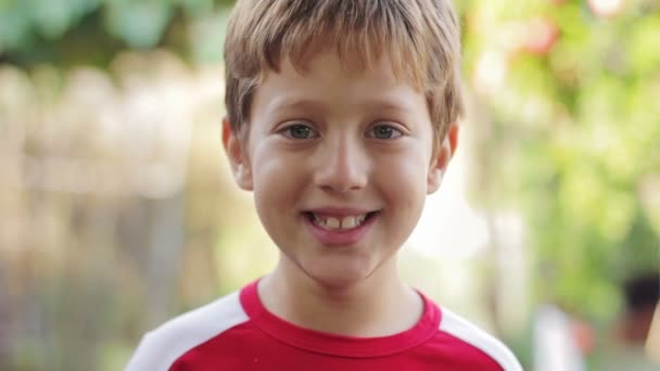 Портрет щасливого радісного маленького хлопчика, який посміхається в парку — стокове відео