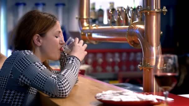 Depressed young woman sitting alone in a pub and drinking alcohol — Stock Video