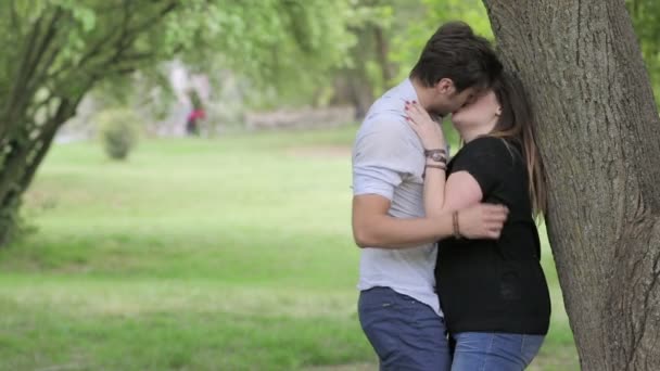 Twee jonge mensen kussen in een openbaar park onder een boom: paar verliefd, minnaars — Stockvideo