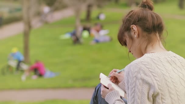 Belle jeune femme écrit un journal en plein air dans le parc : — Video