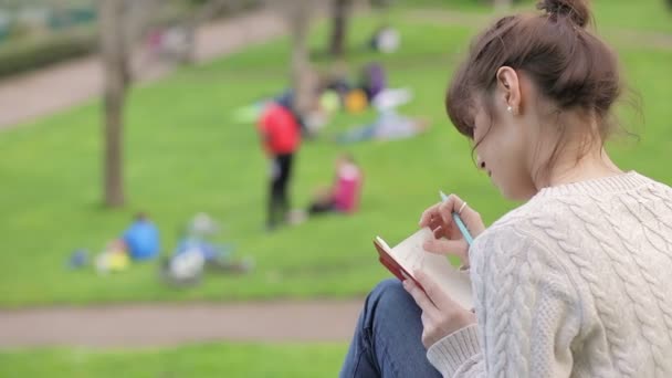 Vacker ung kvinna skriva en dagbok utomhus i parken: — Stockvideo