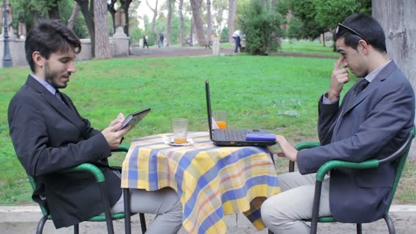 Dos hombres de negocios mirando tableta y portátil durante el desayuno de negocios — Vídeos de Stock