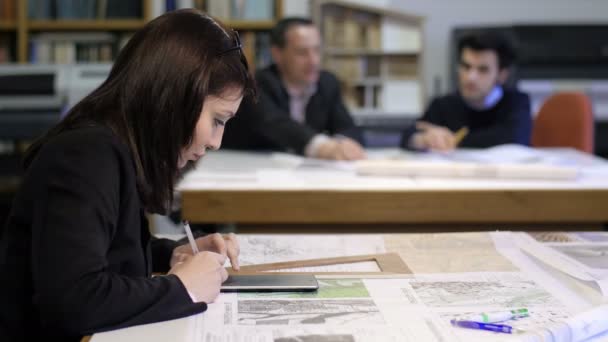 Mujer arquitecta trabaja con calculadora y colegas hablando en segundo plano — Vídeo de stock