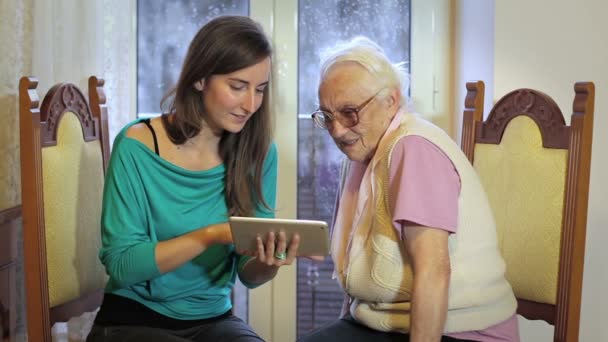 Junge Frau lehrt Seniorin, wie man einen Tablet-PC benutzt — Stockvideo