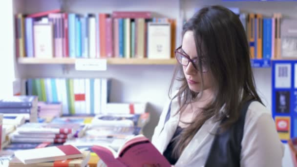 Hermosa mujer leyendo un libro en una librería — Vídeos de Stock