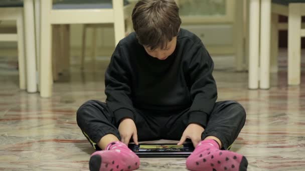 Child plays video games with a tablet sitting on the floor — ストック動画