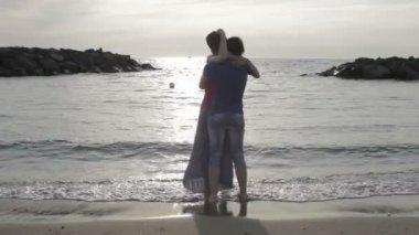 bir erkek ve bir kadın dans ve deniz kenarında günbatımında sarılma