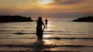 aşık giyimli kadın erkeğini için deniz - hugs ve öper - gün batımına doğru çalışır.