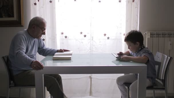 Nonno legge un libro mentre il bambino legge un ebook con il suo tablet — Video Stock